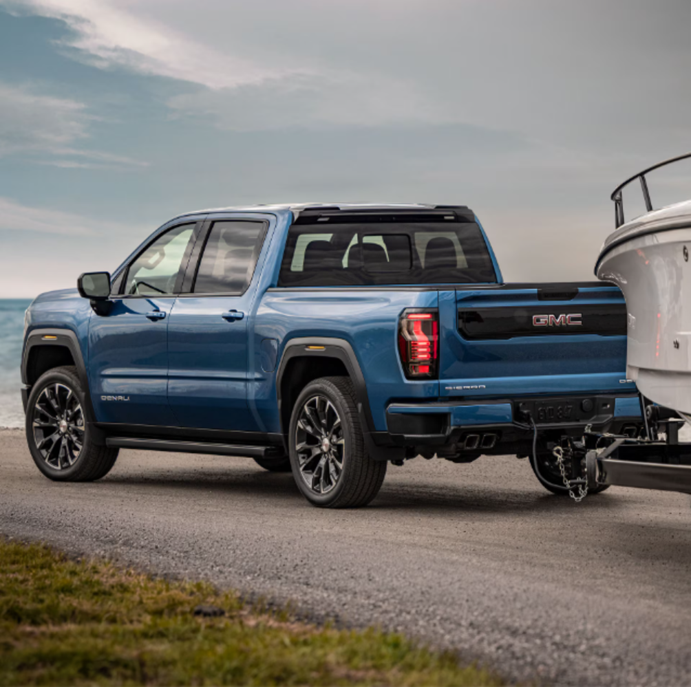 A blue GMC Sierra 1500 towing a boat while driving on the road.