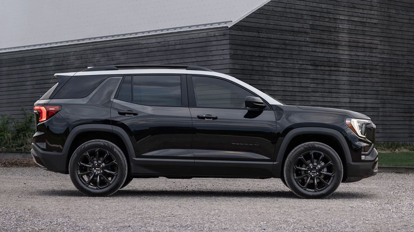 A black GMC Terrain parked on a dirt road in front of a dark grey barn.ALT