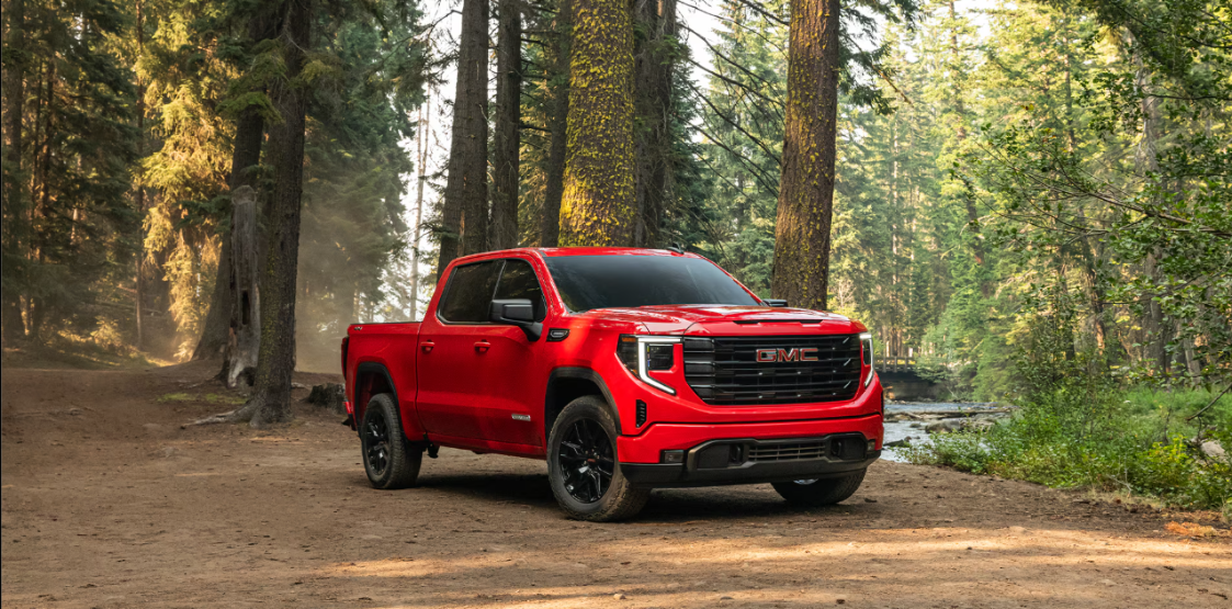 A red GMC Sierra 1500 in a forest on a dirt road.