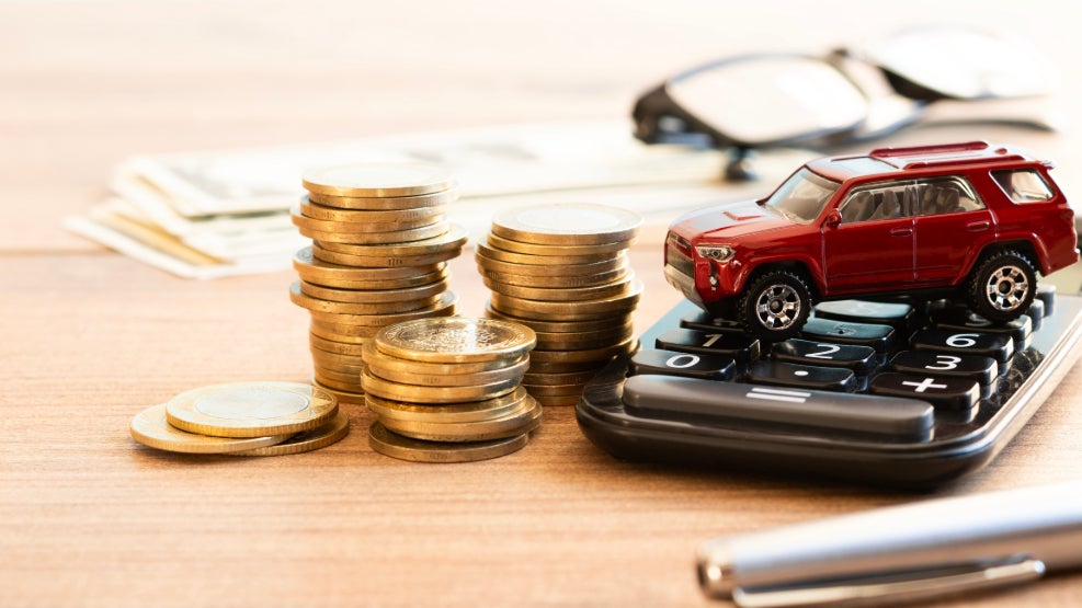 A stack of gold coin dollars next to a calculator with a red toy car on it, and paperwork in the background.