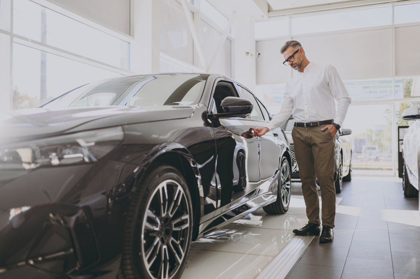 A man examining a black car in a dealership.